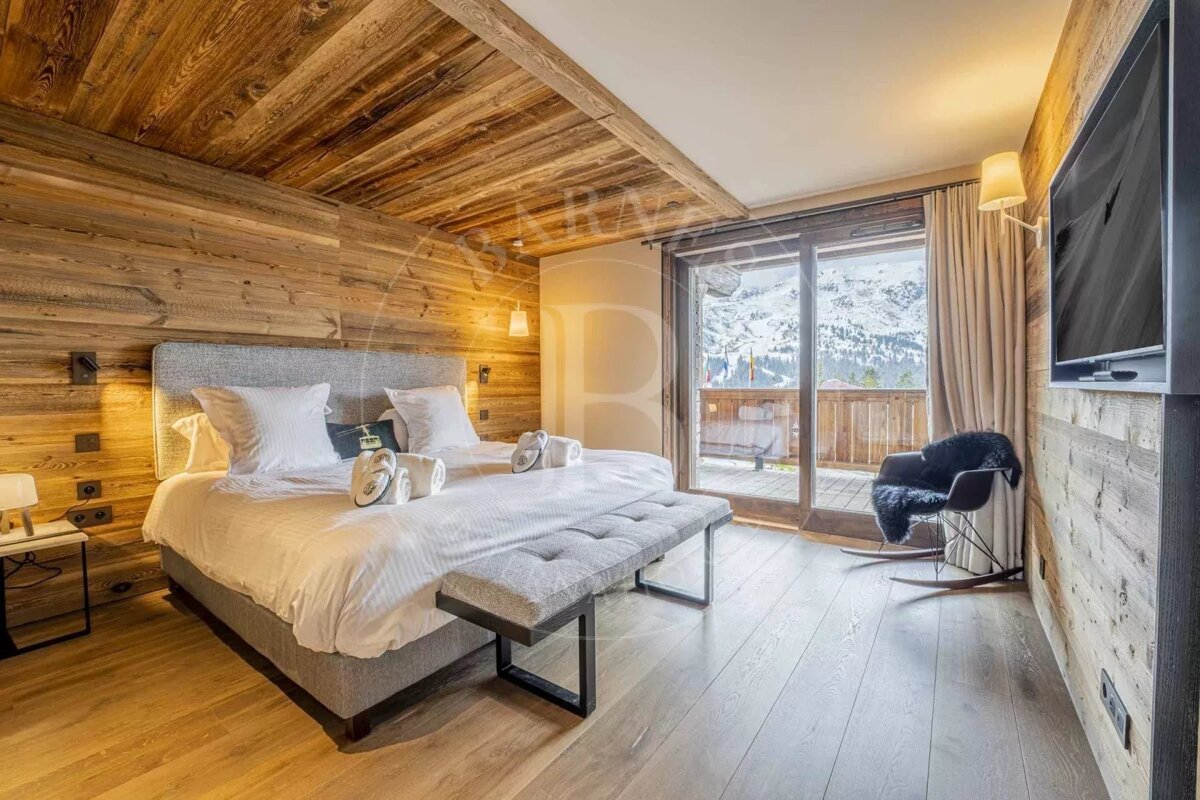 A cozy, modern bedroom with wood walls/ceiling, a large bed, light wood floors, and a balcony revealing a snowy mountain view. Includes a rocking chair.