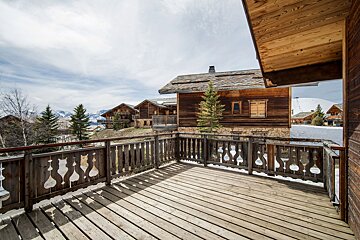 Wooden balcony overlooking rustic alpine chalets in a snowy mountain setting.