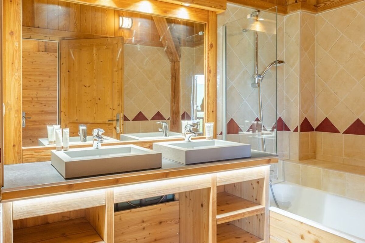 Rustic wooden bathroom with a double vanity, rectangular sinks, a large mirror, and a tiled bathtub with a glass-enclosed shower.