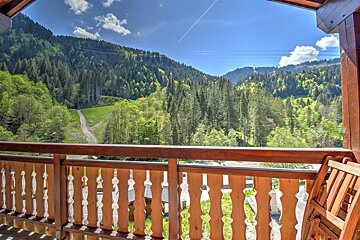 Wooden balcony overlooking a lush green pine forest on mountain slopes under a clear blue sky.