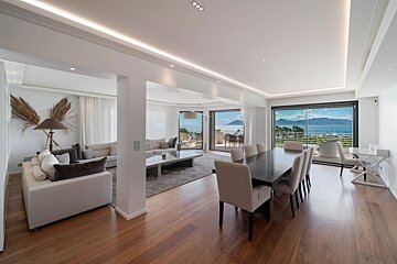 Spacious, modern living and dining room with a beautiful sea and mountain view from large windows, featuring hardwood floors.
