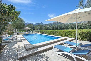 A large swimming pool surrounded by chairs and a white umbrella