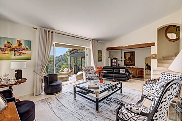 A stylish living room featuring black-and-white patterned armchairs, a glass coffee table, and large glass doors opening to a balcony.