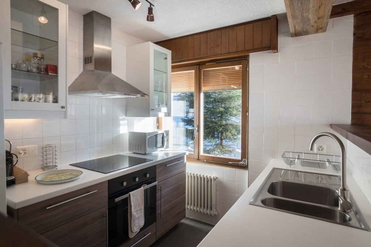 Bright modern kitchen with white tiles, wood cabinets, stainless steel appliances, and a window overlooking a snowy landscape.
