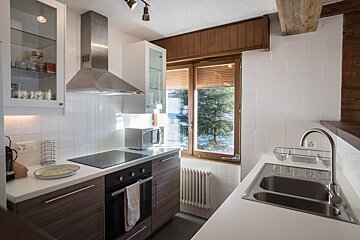 Bright modern kitchen with white tiles, wood cabinets, stainless steel appliances, and a window overlooking a snowy landscape.