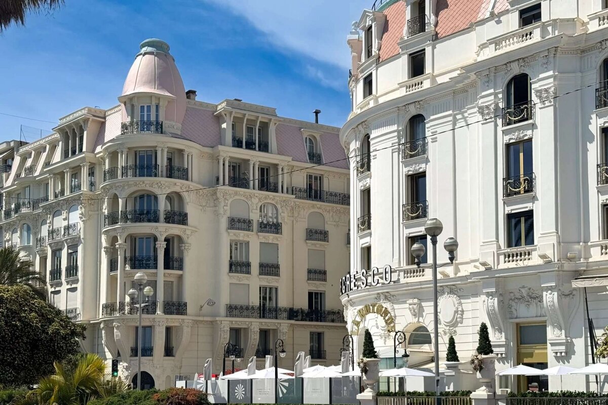 Two ornate white buildings with pink roofs and balconies against a blue sky. One reads 