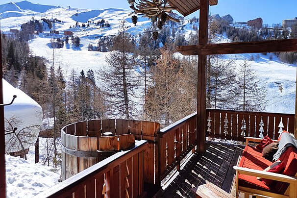 A balcony overlooking a snowy mountain with a wooden tub in the foreground