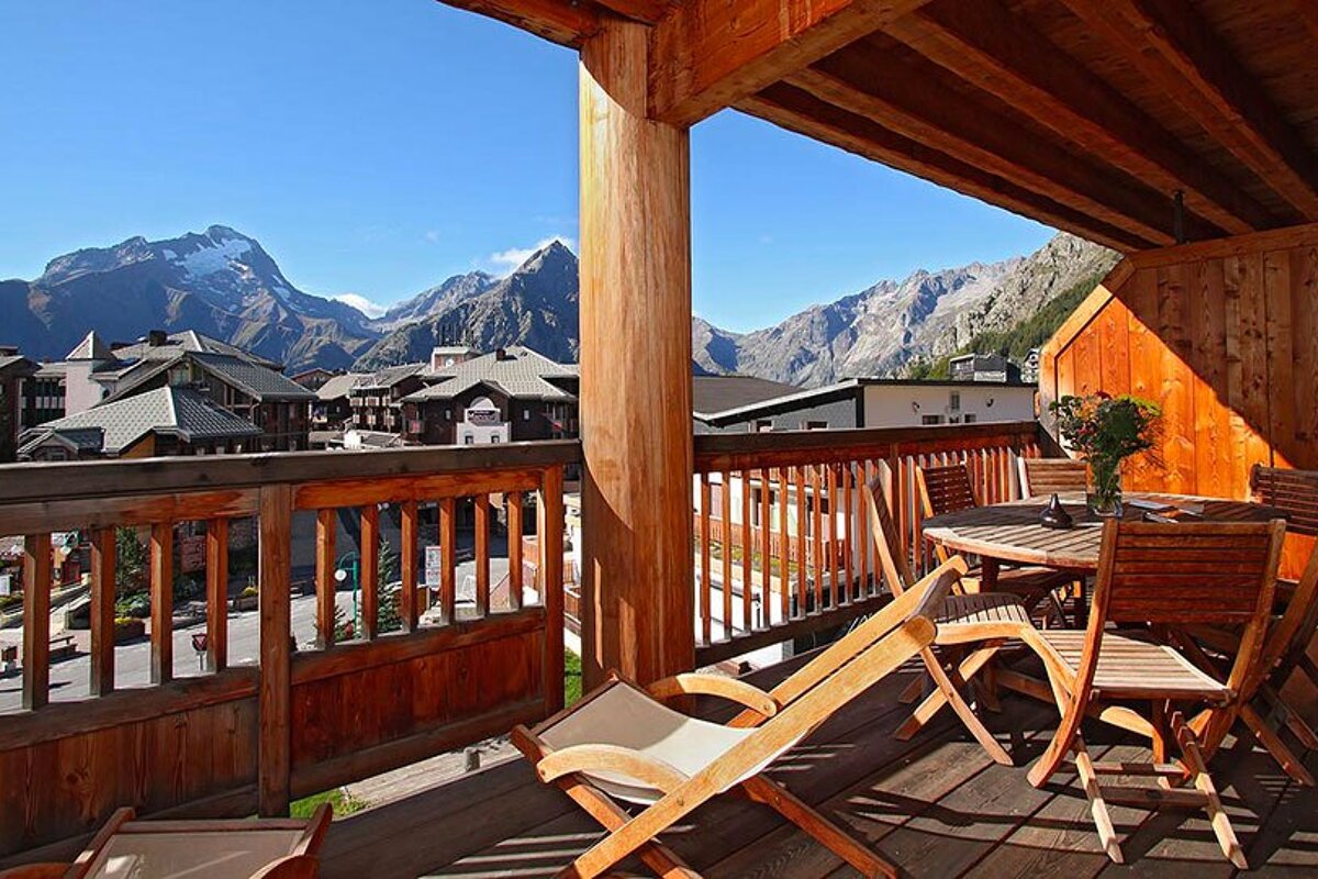 A balcony with chairs and a table with mountains in the background