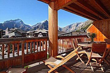 A balcony with chairs and a table with mountains in the background