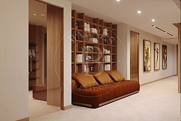 A modern interior features a brown sofa in front of a large wooden bookshelf. A well-lit hallway with artwork extends to the right, and a wine rack is visible through a glass partition.