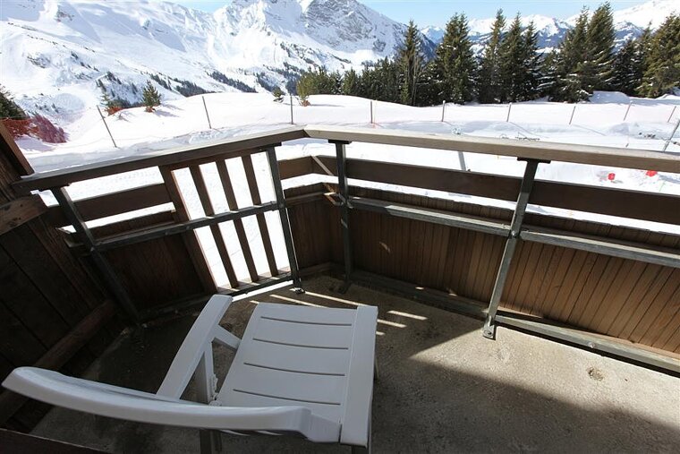 A white chair sits on a balcony overlooking snow covered mountains