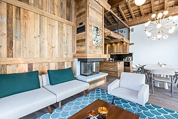 Modern chalet interior featuring wood-paneled walls, a fireplace, contemporary furniture, a blue patterned rug, and a dining space.