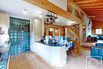 Rustic cabin interior with an open-plan kitchen, exposed wooden beams, a glass block wall, and a living area.