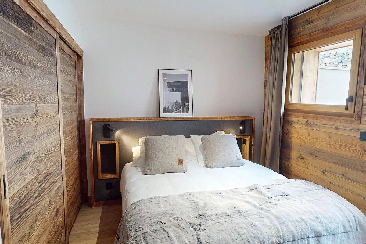 Cozy rustic bedroom with a double bed, warm lighting, wooden paneling, and a sliding wood closet door.