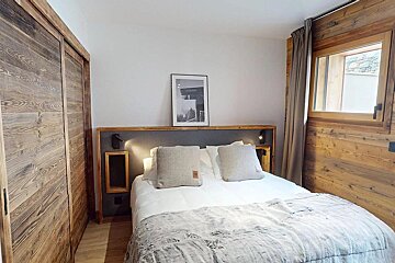 Cozy rustic bedroom with a double bed, warm lighting, wooden paneling, and a sliding wood closet door.
