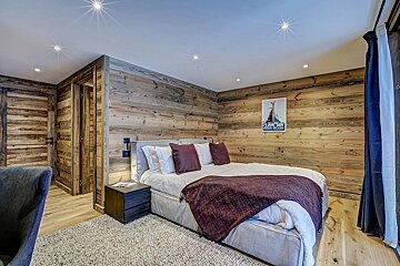 Cozy bedroom with rustic wooden walls and floor, featuring a bed with maroon and white bedding, a ski poster, and modern ceiling lights.