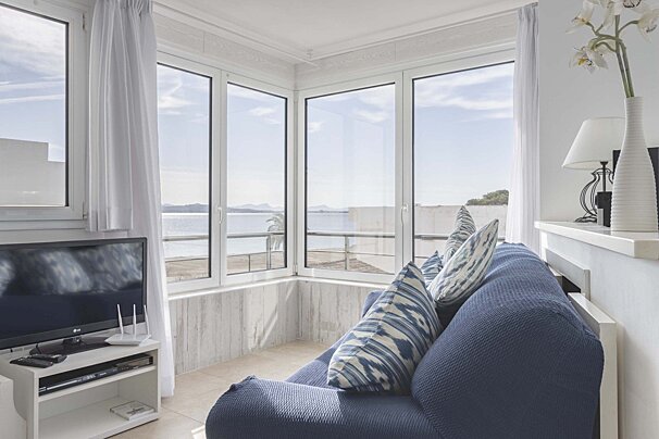 A cozy living room with a blue sofa, large windows showcasing a beautiful ocean view, a TV, and white decor.