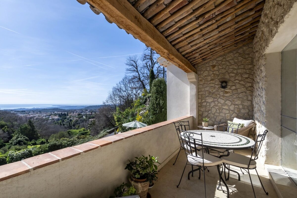 Rustic terrace with stone walls, a dining set, and a stunning view of rolling hills and the sea under a clear blue sky.