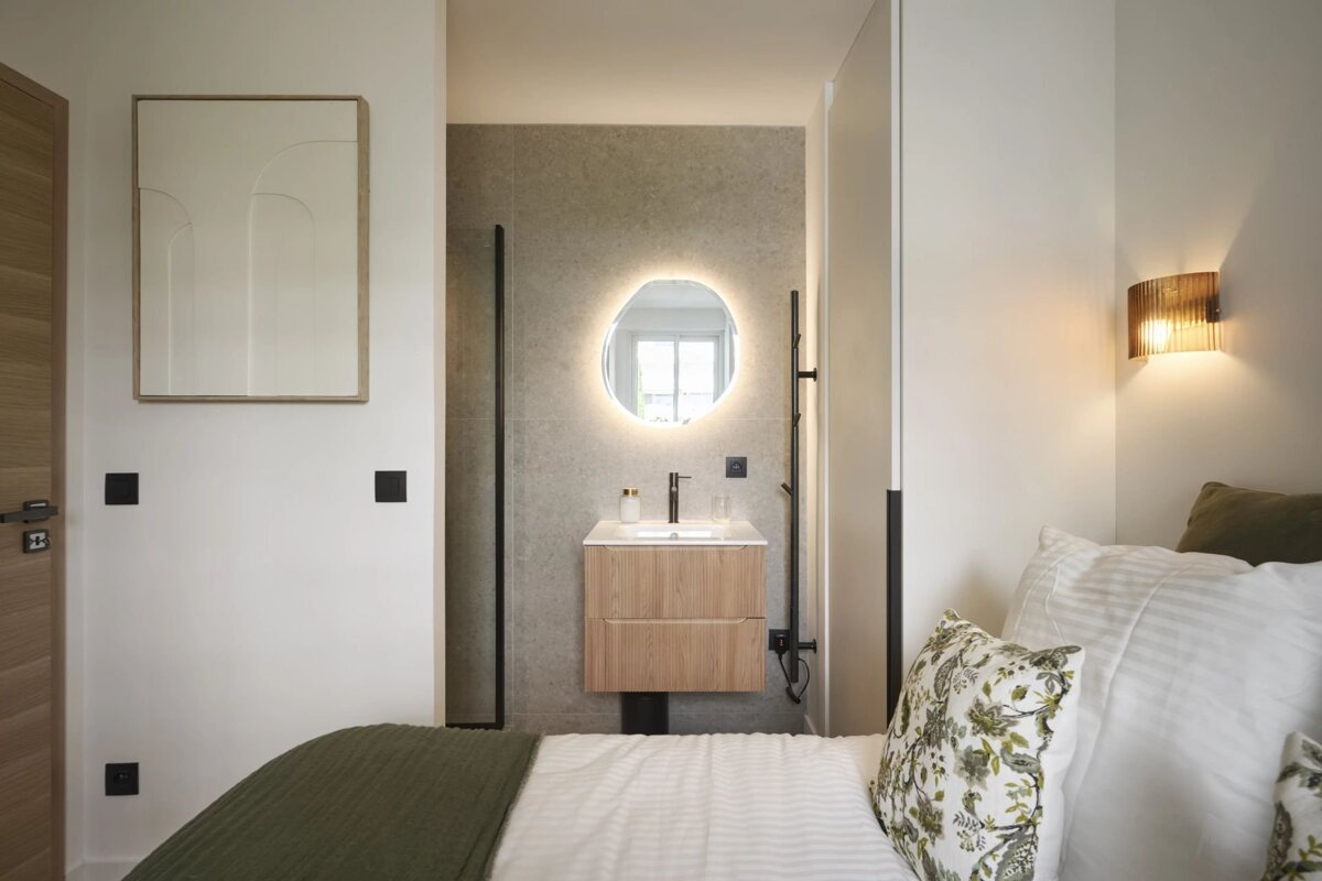 Sleek bedroom with an integrated modern vanity and backlit mirror, featuring a bed with green and white bedding.