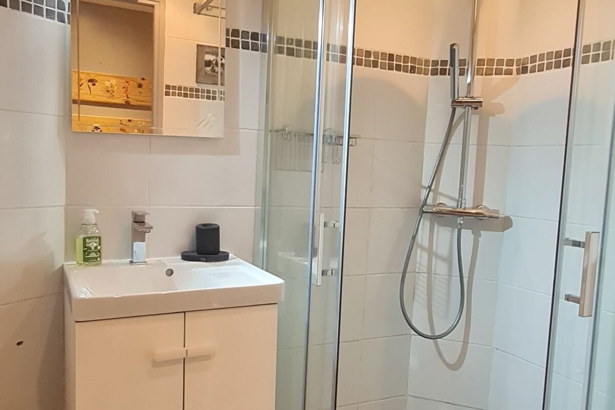 A clean bathroom featuring a white vanity sink, a mirror, and a glass-enclosed shower cabin with white tiled walls.