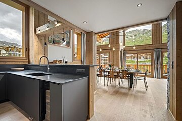 Modern open-plan kitchen and dining area in a wooden chalet, featuring large windows with stunning mountain and village views.