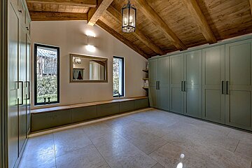 A room with a vaulted wooden beamed ceiling, light green built-in cabinets, a tiled floor, windows, and a mirror above a storage bench.