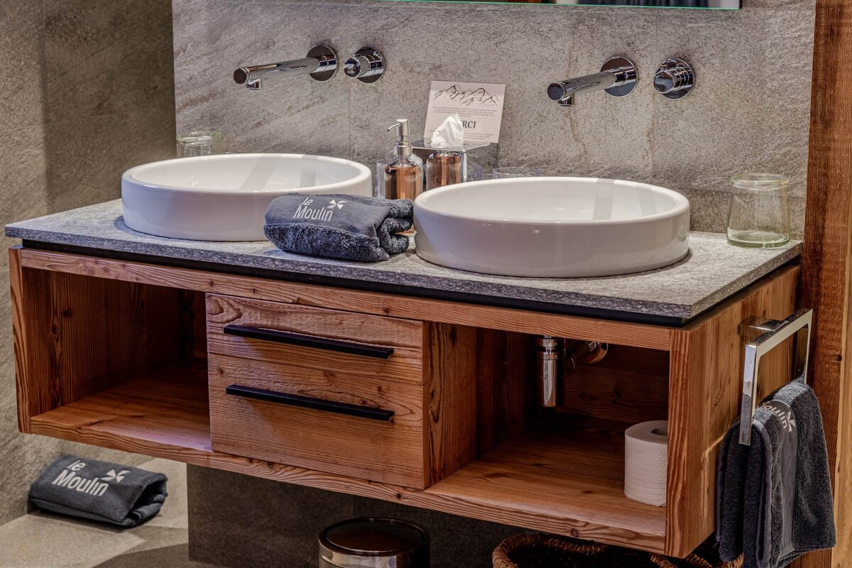 A rustic modern bathroom vanity with dual white vessel sinks, chrome wall faucets, and a floating wooden cabinet.