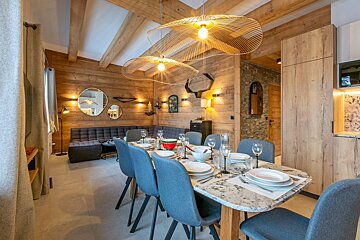 Modern chalet dining room with a set table, blue chairs, warm wooden walls, unique pendant lights, and a cozy lounge area.