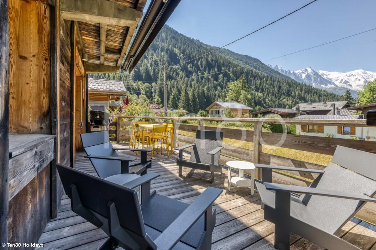 A balcony with chairs and a table with mountains in the background