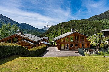 Beautiful wooden alpine chalets nestled in a lush green mountain valley beneath a bright blue sky.