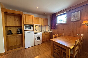Cozy, rustic kitchen and dining area with wooden paneling, cabinets, a table with chairs, a small fridge, and a washing machine.