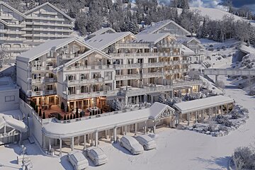 A rendered luxury chalet complex or hotel, snow-covered in a winter mountain landscape, with warm interior lights and parked cars.