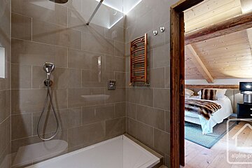 A sleek, tiled shower area with a towel warmer, adjacent to a cozy bedroom featuring a sloped wooden ceiling and a bed with a fur throw.