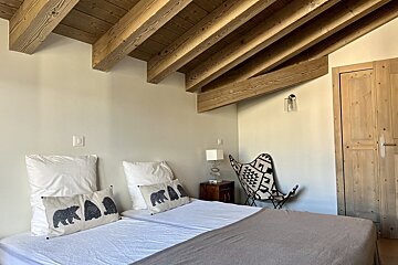 Cozy bedroom with two single beds, bear pillows, and a wooden beamed ceiling. A geometric patterned butterfly chair adds a stylish touch.