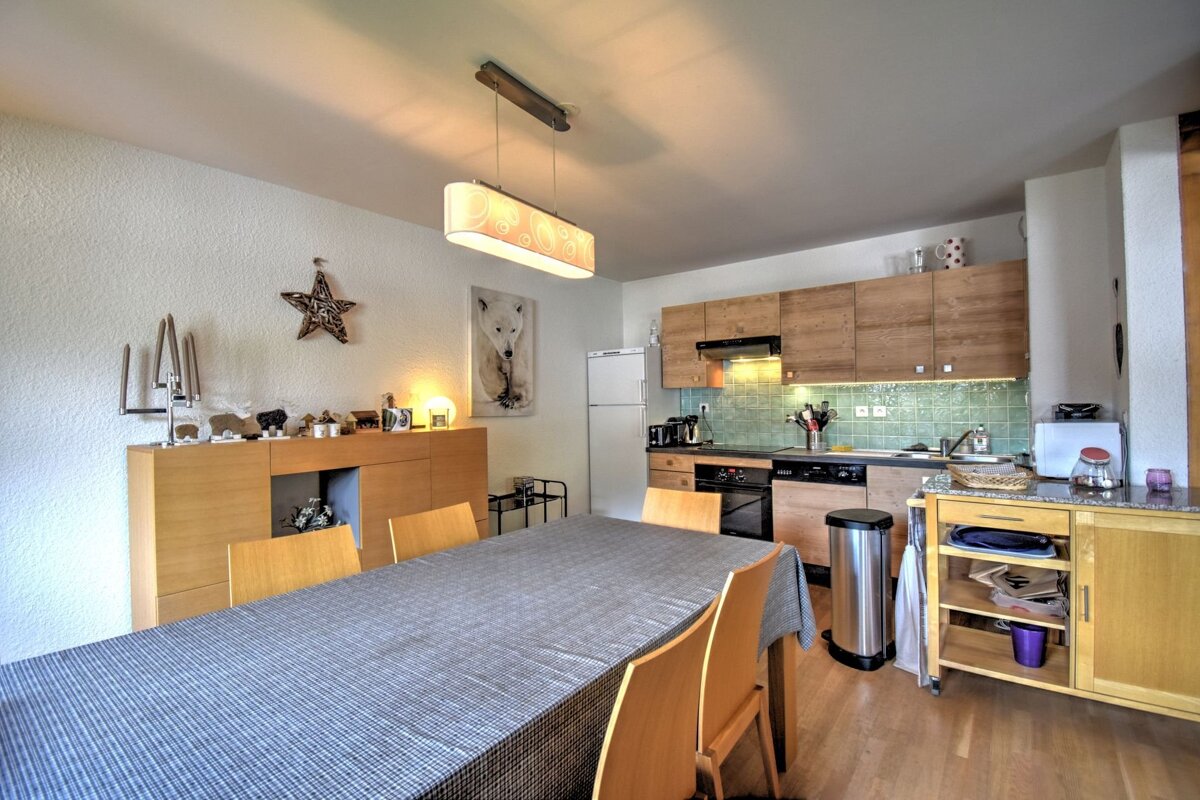 Cozy open-plan kitchen and dining room featuring light wood cabinetry, a long table, and warm decor like a polar bear print and star.