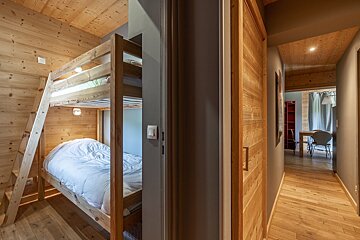 A wooden bunk bed in a hallway next to a desk