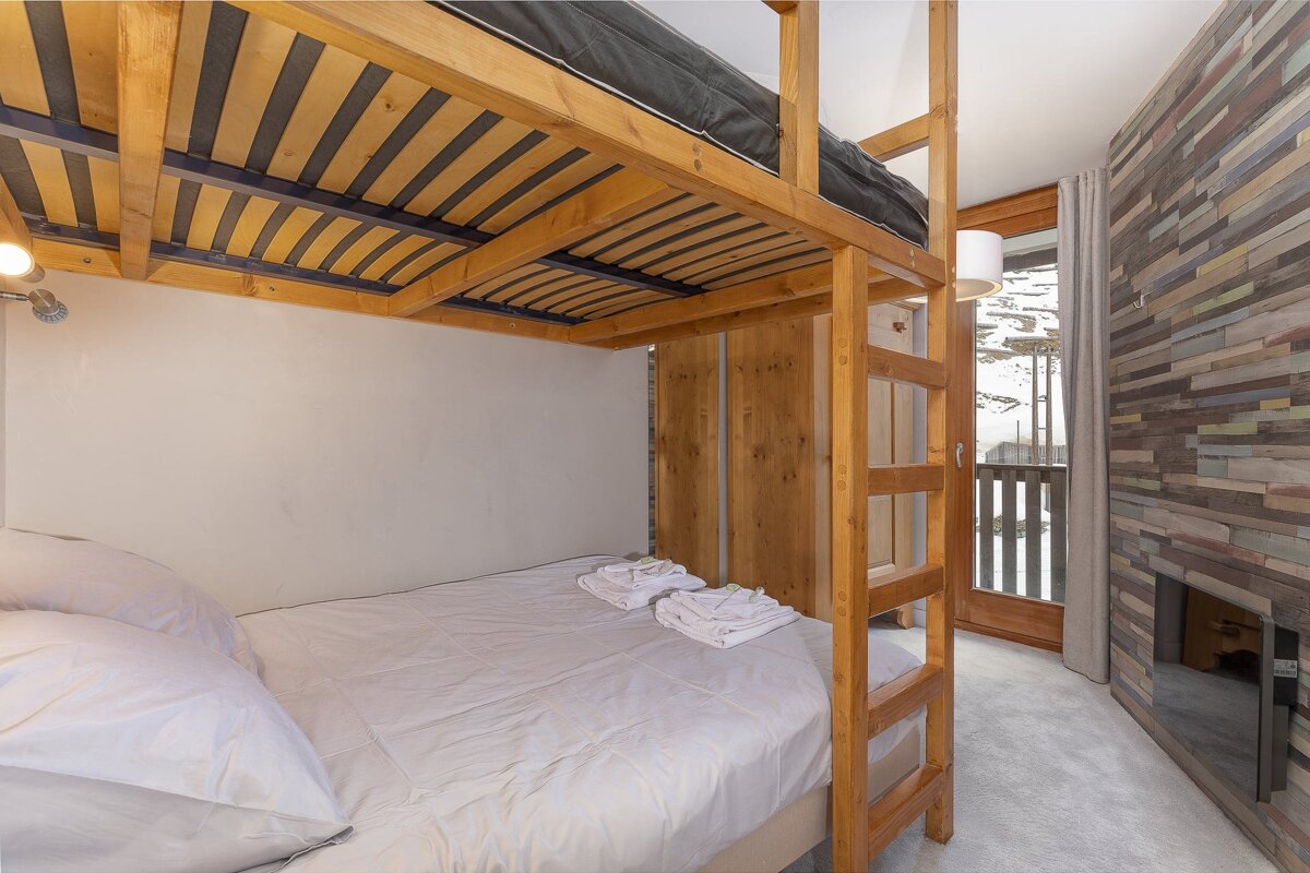 A cozy cabin bedroom featuring a wooden bunk bed with a double bed on the bottom, a textured wall, and a balcony view.