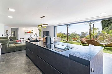 Sleek open-plan kitchen and living area, connected to a vibrant outdoor garden with palm trees and stylish patio seating.