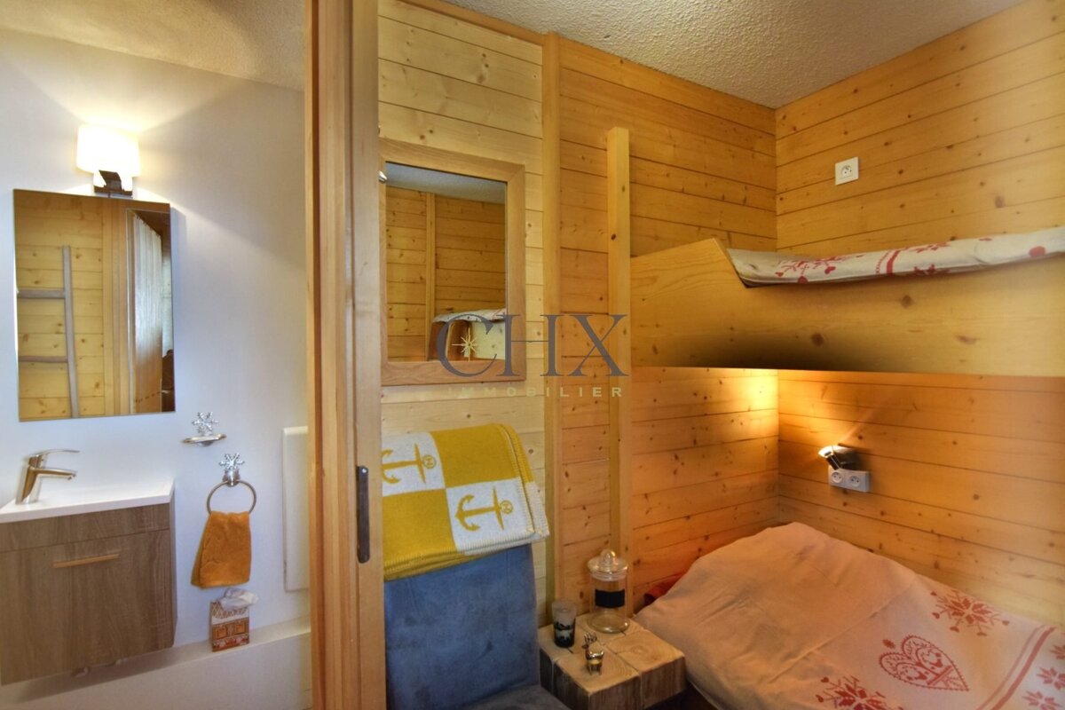 Cozy wood-paneled chalet bedroom with built-in bunk beds, adjacent to a compact bathroom with a modern sink and mirror.