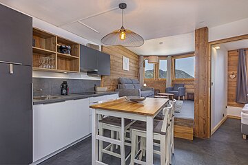 A modern alpine apartment featuring a sleek kitchen, a wooden dining table, and a cozy living room with mountain views.