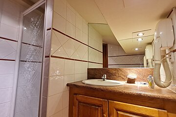 A tiled bathroom featuring a glass shower, wooden vanity with a sink, large mirror, and a wall-mounted hairdryer.