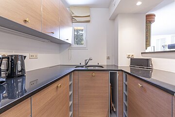 Modern U-shaped kitchen with light wood cabinets, dark countertops, a sink, kettle, toaster, and a window overlooking greenery.