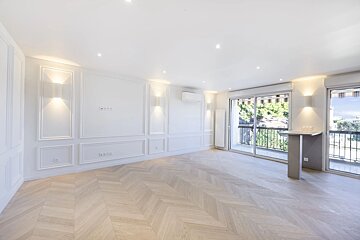 Empty room with white paneled walls, herringbone parquet floors, warm wall sconces, and sliding doors leading to a balcony.