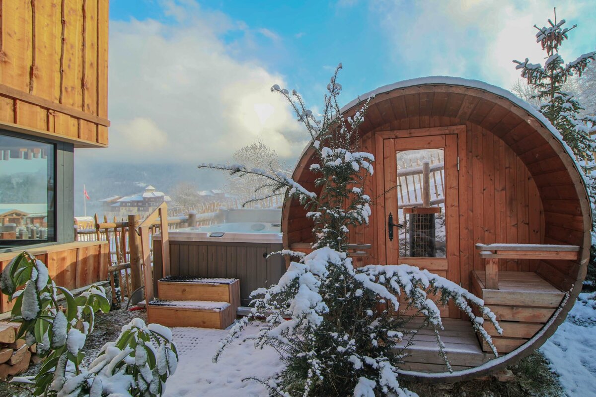 A wooden barrel in the snow with a hot tub in the background