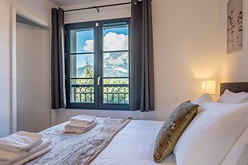 Cozy bedroom with a bed in the foreground and a large window showcasing a beautiful mountain view.