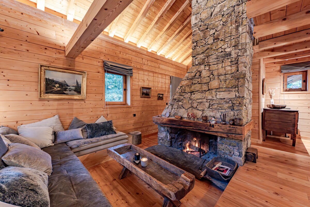 Cozy wooden cabin living room with a large stone fireplace, crackling fire, comfortable sofa, and rustic furniture. Warm and inviting atmosphere.