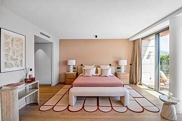 Modern bedroom with a pink accent wall, a scalloped rug, neutral decor, and large glass doors opening to a bright patio.