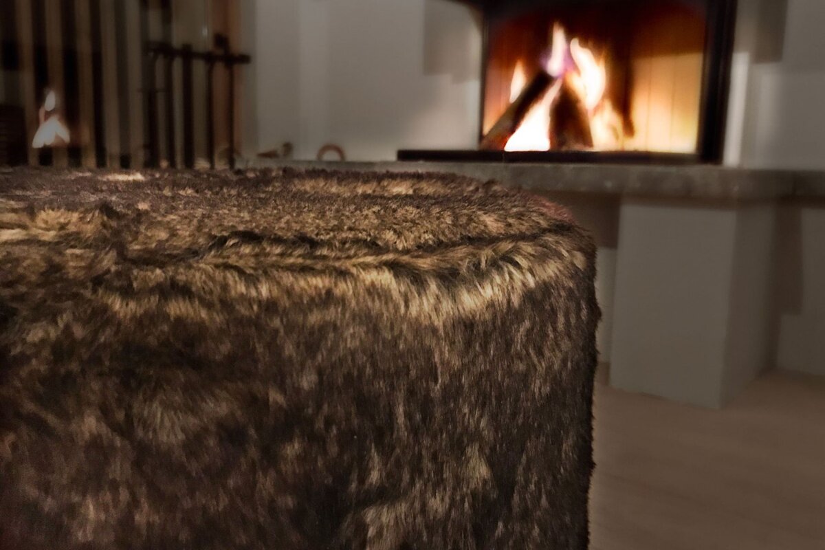 A furry ottoman sits in front of a fireplace