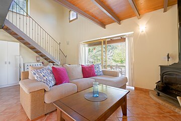 A bright living room features a beige sectional with colorful pillows, a wooden coffee table, tiled floor, staircase, and sliding doors to outdoors.