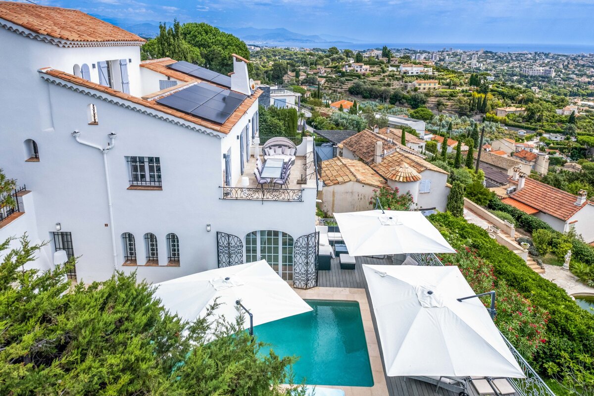 A large white house with a pool and umbrellas in front of it
